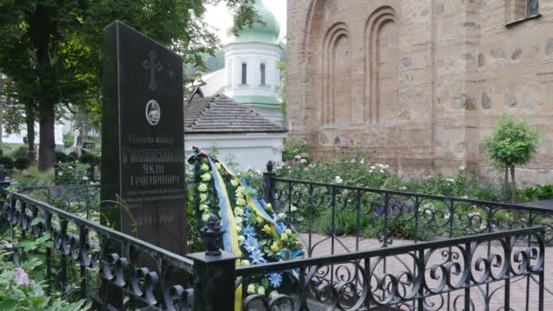 Monumento a la Tumba de Mármol en el Patio Monasterio Vydubychi Hombres Monasterio Corona se coloca en una tumba decorada con cinta azul y amarilla Iglesia de la pared de ladrillo rojo — Vídeo de stock