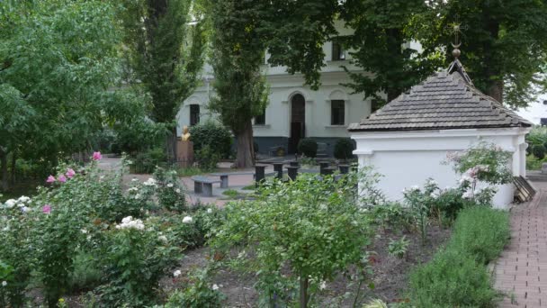 Bloemen steeg struiken in de binnenplaats Vydoebytsji mannen klooster witte kleine verlaten gebouwen weelderig groene bomen in een tuin bestrating stenen voetpad in een steegje — Stockvideo