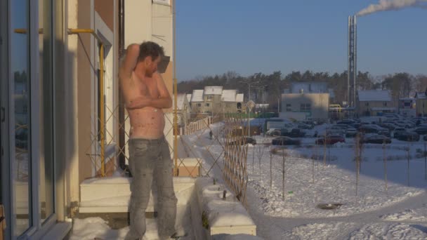 Человек растирает свое тело снегом на балконе Солнечный день Человек с бородой среднего возраста мужчина раздетый до пояса на балконе своей квартиры в зимнее время — стоковое видео