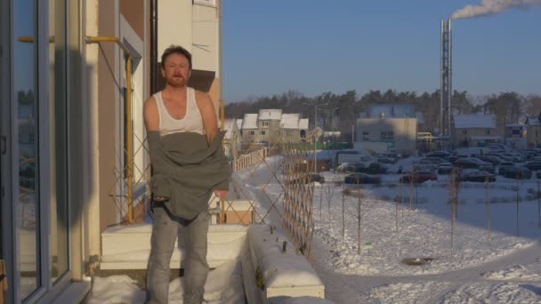 Homem esfrega seu corpo com neve na varanda homem com barba leva fora sua camisola Man é despojado até a cintura na varanda de seu apartamento, em um tempo de inverno — Vídeo de Stock