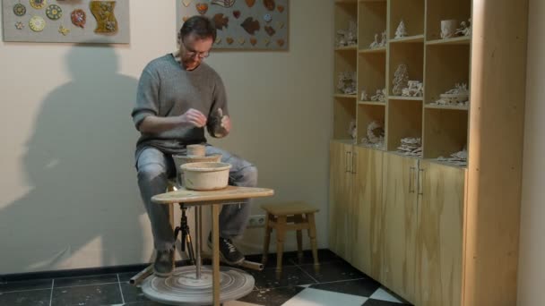 L'homme moulant un pot d'argile met ses mains dans l'eau Travailler à une roue de poterie Rotation d'une roue avidement étudiant apprend un atelier de poterie artisanale — Video