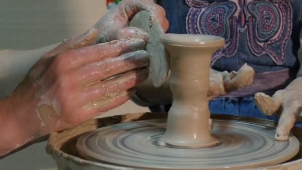 Enfant et enseignant moulent sur la roue de poterie Les mains de la femme forment un vase avec spatule Dirty Kid mains Jeans Tablier roue est rotatif atelier de poterie — Video