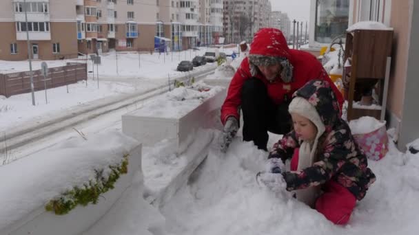 Ребенок и отец сидят на снегу и заставляют Снеговика папа и дочь играют со снегом вместе Фигура сделана из снега семья отдыхает облачно день — стоковое видео