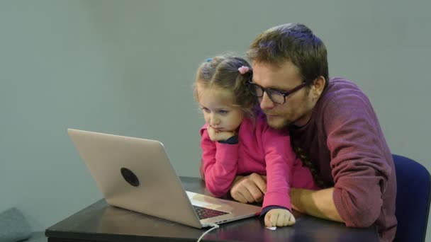 Vader en kind kijken video in Internet Dad vraagt het meisje Kid antwoordt leert zijn dochter om te werken met laptop man en Kid zitten aan tafel — Stockvideo