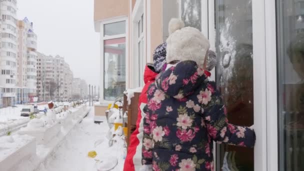 Muž nakreslí obraz na skleněném otci třesknout sníh z dětské boty hrající si se sněhem na Cornice otec a jeho dcera Vstupte do domu skrz okno — Stock video