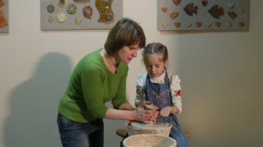 Tekerlek sarışın küçük kız bir kil kalıp çocuk çanak çömlek çarkı kadın oturuyor öğretmen yardımcı olur söz yıkar Her el ile bir kase su