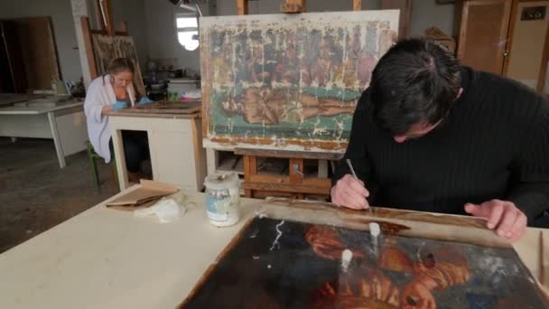 Vrouw Man kunstenaars in hun Studio werk pictogrammen restauratie orthodoxe beelden reparatie winkel restauratie groep in Kiev Man aan de tafel schilderen van een beeld van Jezus — Stockvideo