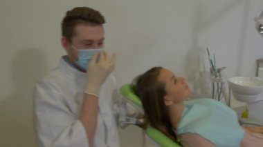 Diş hekimi olduğunu konuşan bir kadın istemciye gülümseyen üzerinde yeşil sandalye doktor bir laboratuvar kat maske ve eldiven inceleyerek bir diş diş tedavi odası oturuyor