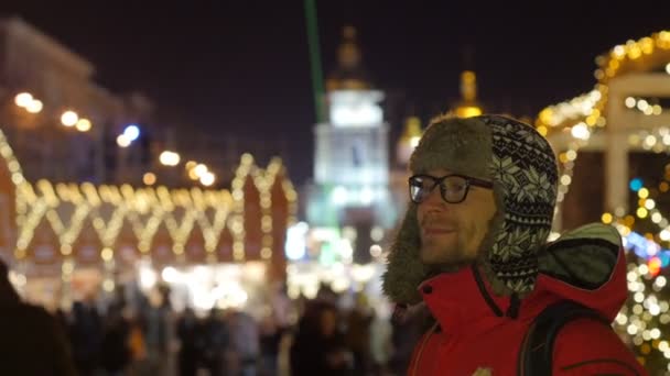 El hombre está sonriendo viendo algo Nochebuena en la noche de Año Nuevo de abeto decorado cuadrado en una plaza de Sofía y la celebración de la plaza Mikhailovskaya — Vídeo de stock