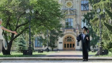 Genç kadındır Hugging manto gülümseyen Graduand öğrenci Walking Away From Üniversitesi eski tuğla bina çevrili ile Park yeşil ağaçlar olduğunu