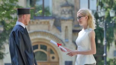 Teacher Gives a Diploma to Graduand Young Man Smiling Shows the Diploma Walks Away Ceremony Alley Outside the Univesrsity Sunny Summer Day Green Trees