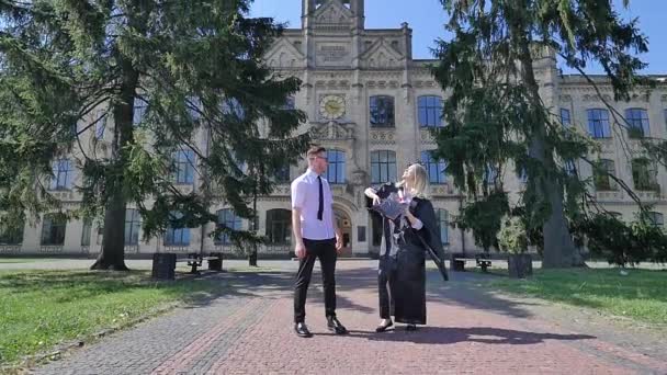 Absolventen haben Spaß Frau im Mantel wirft Hut auf lächelnden jungen Mann zu Fuß entlang der Frau in der Gasse vor der Universität paar Studenten sonnigen Tag — Stockvideo