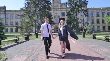 Mantoda El Ele Tutuşan Mutlu Graduands Çift Gömlek adam twisting ve Tie Üniversite Sunny Yaz Günü Dışında Alley Yürüyüş