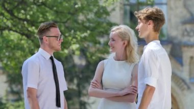 Üç Arkadaş Güneşli Gün Öğrenciler Erkek ve Kadın Beyaz Giyinmiş Eski Bina Park Alley Yeşil Ağaçlar Avlu gülümseyen Gesticulating konuşuyoruz