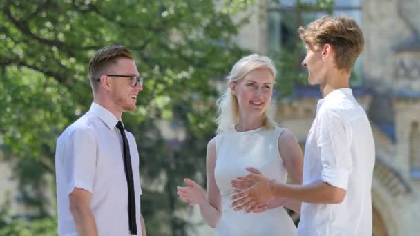 Freunde unterhalten sich lächelnd gestikulierendes Lachen zeigt ihre Daumen beim Bau von Parkallee grünen Bäumen an sonnigen Tagen Studenten Männer und Frauen in weiß gekleidet — Stockvideo