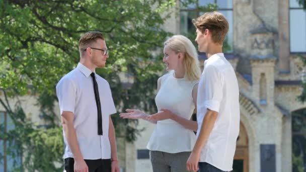 Junge Leute sprechen junge Männer, die lächelnd Hände schütteln und eine Übereinkunft treffen, die mit einer Frau im Hof alter Baufreunde im Park steht — Stockvideo