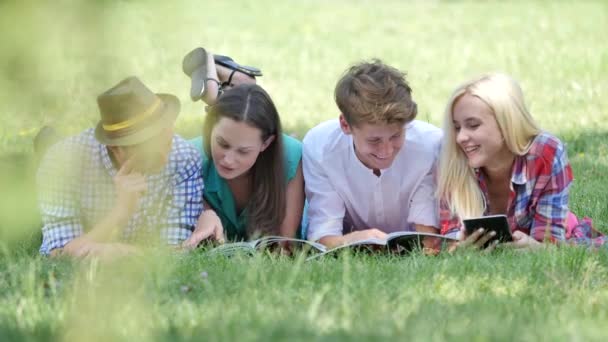 Estudiantes felices leen tumbados en un césped Estudiantes Niñas y niños se preparan para los exámenes Haciendo tareas domésticas en el parque universitario Estudiando en el campus de la naturaleza — Vídeo de stock