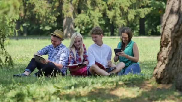 Estudiantes bajo el árbol preparándose para los exámenes al aire libre estudiando lectura Estudiantes Chicas y niños se ríen Haga clic en la tableta que hace el campus de tareas domésticas — Vídeos de Stock