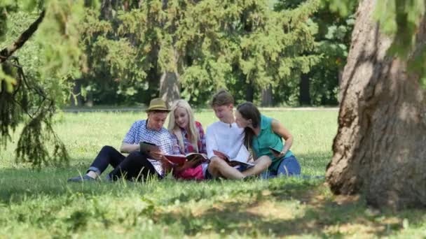 Jovens sentados sob a árvore estudando leitura Estudantes Meninas e meninos estão se preparando para exames que fazem a tarefa de casa no Campus da Universidade da Natureza — Vídeo de Stock