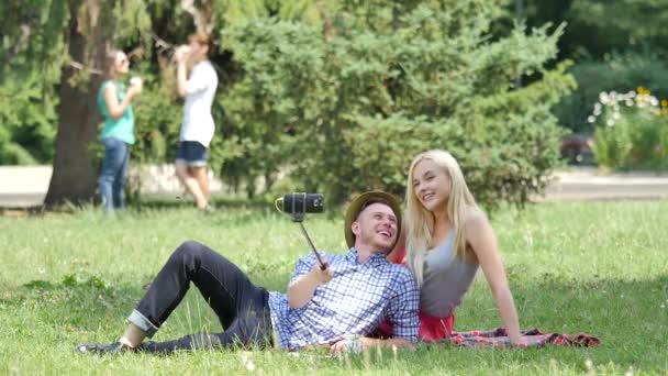 Young Couple on a Picnic in Park Taking Photos Lying on a Green Grass Meadow Teenagers on a Lawn at the Nature Friends Couples Boy and Girl Summer Day — ストック動画