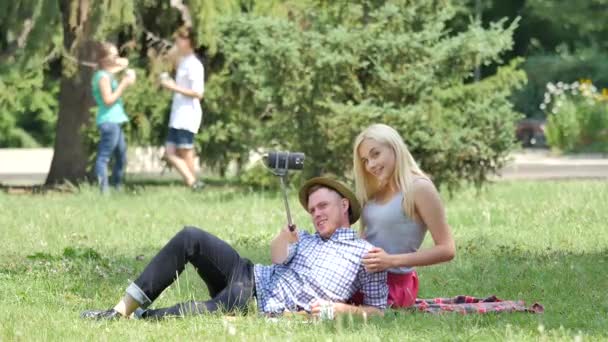 Pareja joven hace un picnic tumbada en un césped Filmando sentada en una hierba verde en el parque Adolescentes en la naturaleza Amigos Parejas pasan tiempo en el soleado día de verano — Vídeos de Stock
