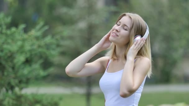 Girl is Listening to Music in Headphones Smiling Gets Pleasure Swaying to the Beat Guy Comes Touches Her Shoulders Girl is Smiling Talking to Him in Park — Stock Video