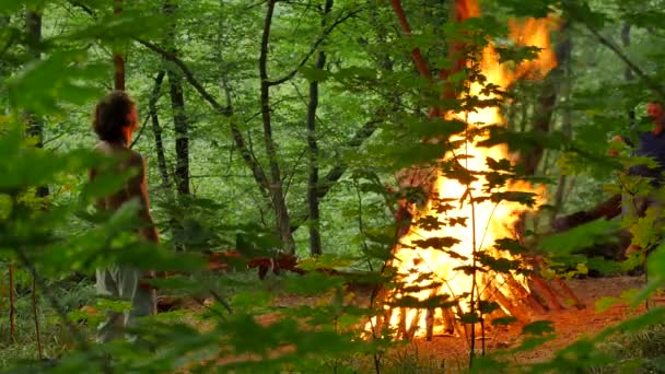 Un bărbat și-a scos cămașa uitându-se la un incendiu aprins Ivan Kupala Pagan Festival Ritual of Bonfire Kindling autentic ceremonie de sărbătoare în pădure copaci verzi — Videoclip de stoc