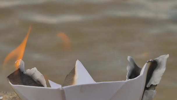 Yanık kenarları kağıt gemi su yüzey hayalleri yanan bir nehir deniz güneşli gün Sandy alt üzerinde doğru kayıp umut ölüm felaket kağıt gemi gelmedi — Stok video