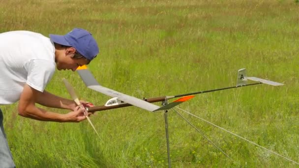 Teenage Boy Preparando su competencia de aviones al aire libre Konotop Ucrania Modelos de arte técnico para niños Ensamblaje Estimación del campo verde del avión Soleado — Vídeos de Stock