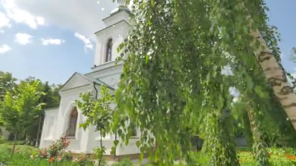 Εκκλησία πίσω από το Πανόραμα σημύδα δέντρο πράσινο ξυλόστεγη εκκλησία αυλή ηλιόλουστη μέρα λουλούδι κρεβάτια δέντρα και γκαζόν λευκό τοίχους καμπαναριό χρυσό τρούλο καλοκαίρι — Αρχείο Βίντεο