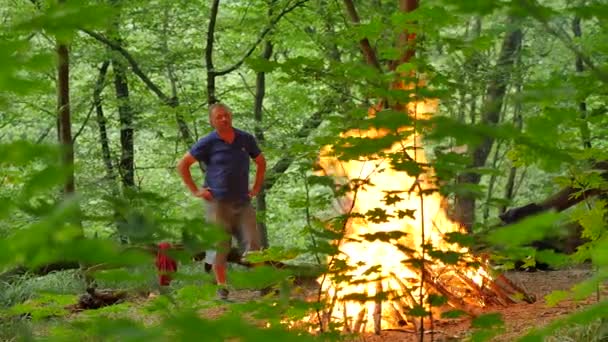 Mensen op de brand in heidense Festival van Ivan Kupala Kiev Man is staande en Looking Bonfire mannen en vrouwen vieren in Forest Green bomen zomer schemering — Stockvideo