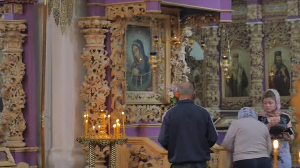 Pessoas na frente de imagens em molduras esculpidas Interior do Mosteiro da Santa Cruz Poltava Trinity Day Iconostasis Sete cúpulas Velas Catedral estão queimando — Vídeo de Stock