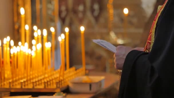 Κληρικοί μπροστά στα κεριά που κατέχουν μια υπηρεσία προσευχής με χαρτί στην εκκλησία της Πολτάβα Ουκρανία εσωτερικό της εκκλησίας κεριά καίνε επιχρυσωμένο διακόσμηση καλόγρια σε μαύρο — Αρχείο Βίντεο