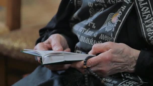 Senior Kvinna håller bön-bok i kyrkan Poltava Ukraina prästerskapet läser en bok nunna i svart kontors plagg band på en mantel med inskriptioner — Stockvideo