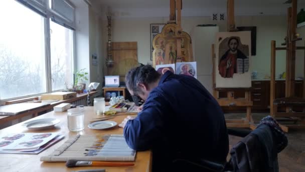 Pintor en gafas lupa está pintando Kiev Día del Trabajador de Arte Restauración de los iconos antiguos Restauración atentamente Grupo Arte Studio Pinceles de diferentes tamaños — Vídeo de stock