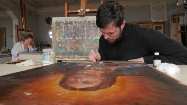 Artistas El hombre está pintando cuidadosamente la restauración de los iconos Kiev Día del trabajo de arte Restauración Grupo Art Studio Mujer en guantes azules La imagen de Jesús Imágenes dañadas — Vídeos de Stock