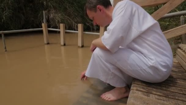 Человек на лестнице на реке Иордан Израиль Крещение Обряд Человек берет воду в бутылку Маленькая болотистая река Деревянные лестницы к зеленой травяной тростник — стоковое видео
