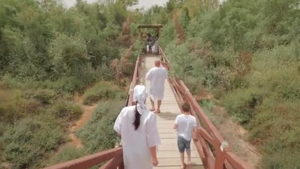 男子妇女孩子步行到约旦河以色列洗礼崇拜者在长白衬衫去沉浸在小沼泽河绿草簧 — 图库视频影像