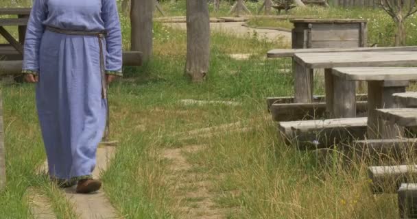 Femme en robe bleue longue, Vêtements anciens de 10-11 siècle, La femme marche par le chemin à côté des tables en bois — Video