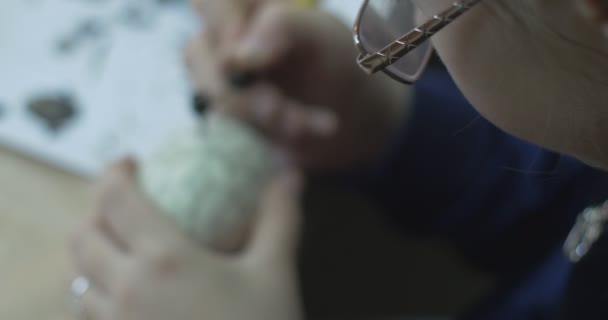 Dívka v modrém svetru a skleničkách maluje na Velikonoce vaječná technika malování na Velikonoce vajíčko velikonoční vajíčko podle náčrtku uvnitř zavřít pohled — Stock video
