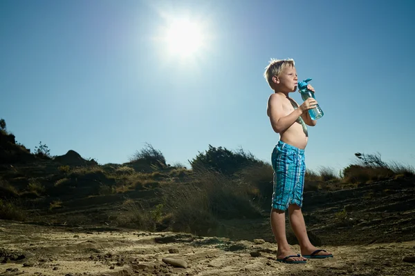 Boy drinking water out of bottle in the desert sun
