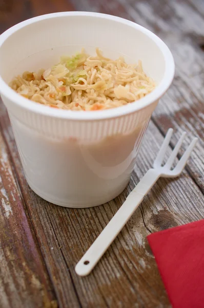 Cup-a-noodles pasta ramen in plastic cup on wood table