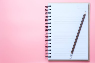 Defter ve kalem pembe bir arka plan üzerinde