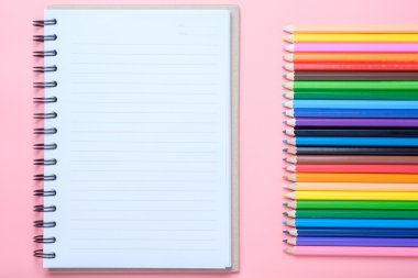 Defter ve pembe bir arka plan üzerinde renkli kalemler