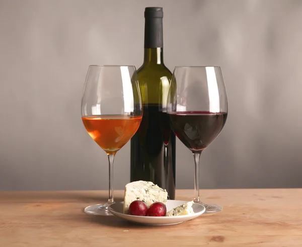 Bodegón refinado de vino, queso y uvas en bandeja de mimbre sobre mesa de madera —  Fotos de Stock