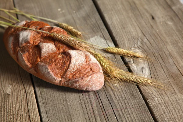 Rustic crusty bread and wheat ears on a dark wooden table — Stock Photo, Image