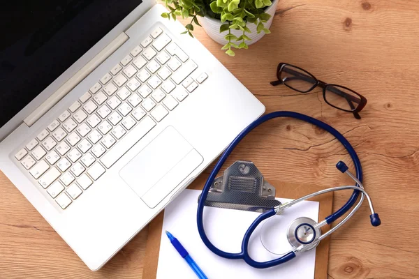 附近一台笔记本电脑上木桌前，在白色的医用听诊器 — 图库照片