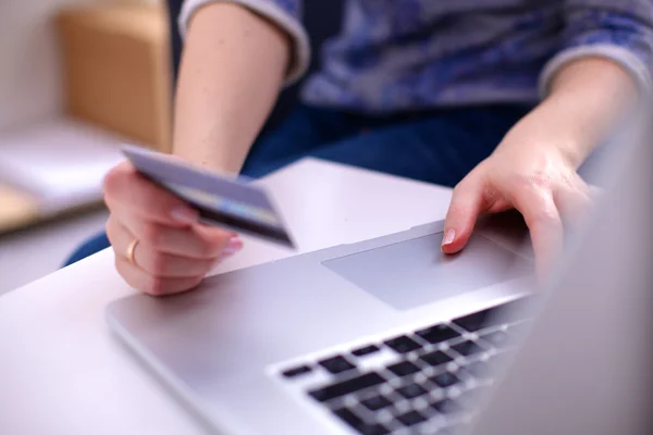 Eller kredi kartını tutuyor ve online alışveriş için dizüstü bilgisayar kullanıyor.