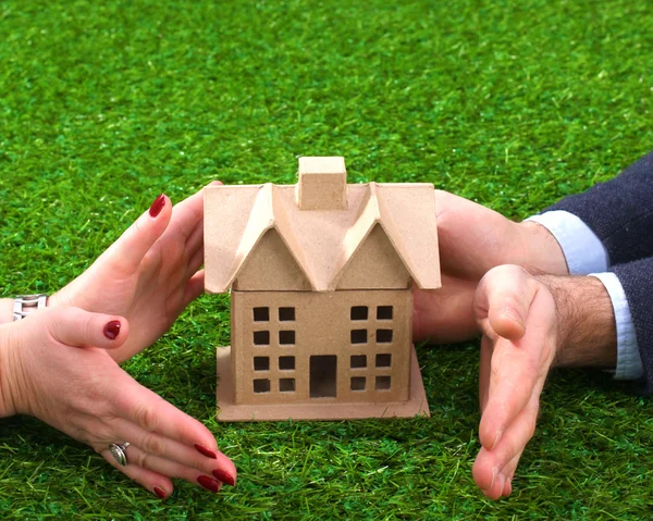 Концепция недвижимости - руки молодой женщины окружают белый дом на зеленой траве — стоковое фото