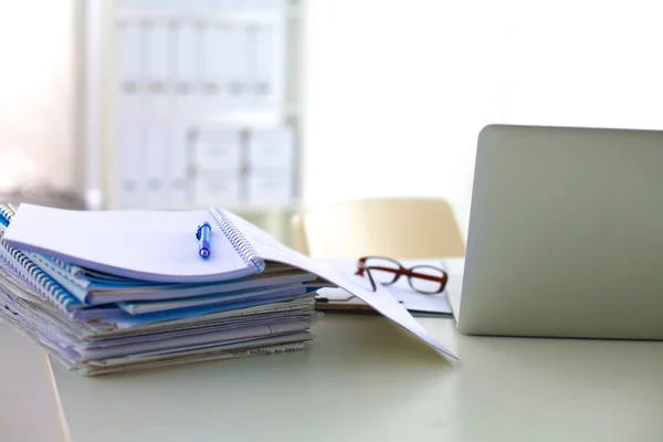 Laptop with stack of folders on table on white background